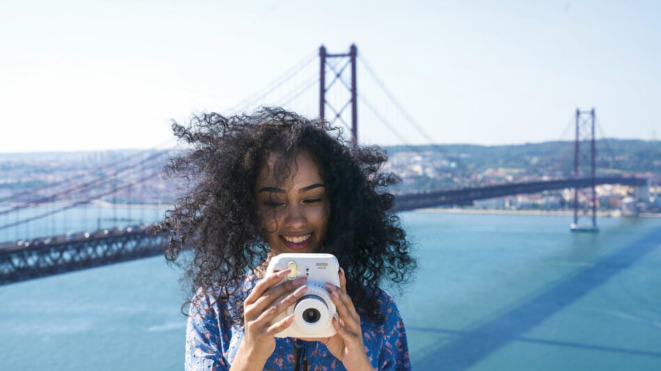 A young woman photographing a bridge in Lisbon, Portugal as part of her travel planning.