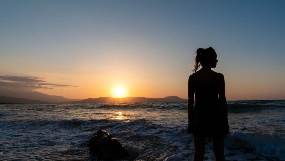 A silhouette of a woman standing on the beach at sunset.