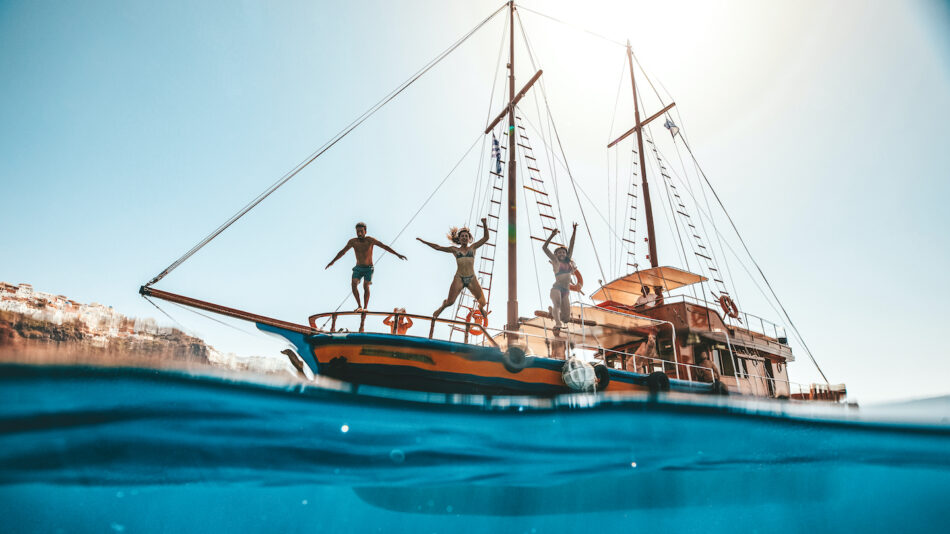 Friends jumping off boat into water having fun in Europe