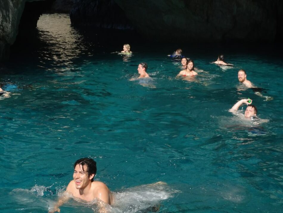 A group of people swimming in the deep blue water of a cave during their travel to Italy.