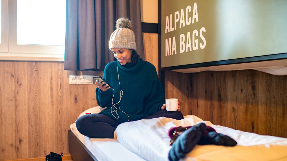 A woman sitting on a bed listening to music after a group ski trip.