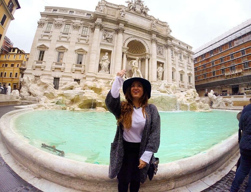 A woman is standing in front of one of the most famous landmarks, the Trevi Fountain.