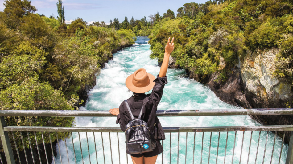 A woman is standing on a bridge overlooking a river in new zealand.