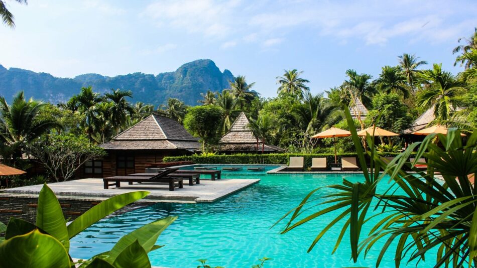 Travel Inspiration: A serene oasis featuring a swimming pool enveloped by majestic palm trees and towering mountains.