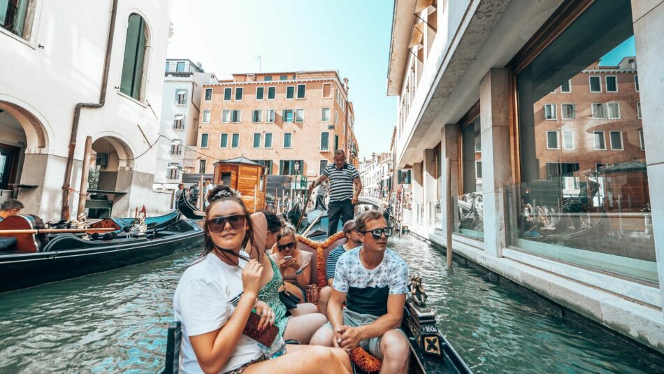 Group of 5 young travellers sit in gondola, floating down Venice canal