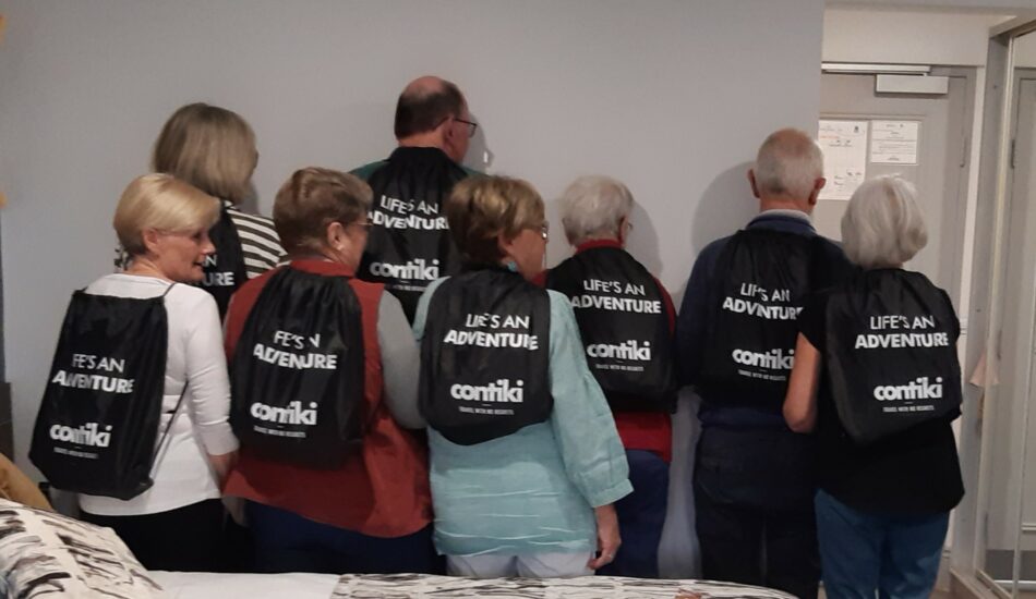 A Contiki reunion with a group of people standing in a room, each wearing backpacks.