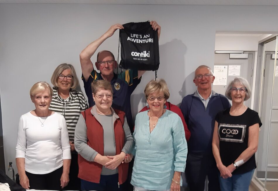 A Contiki reunion where a group of people happily pose for a photo with a bag.