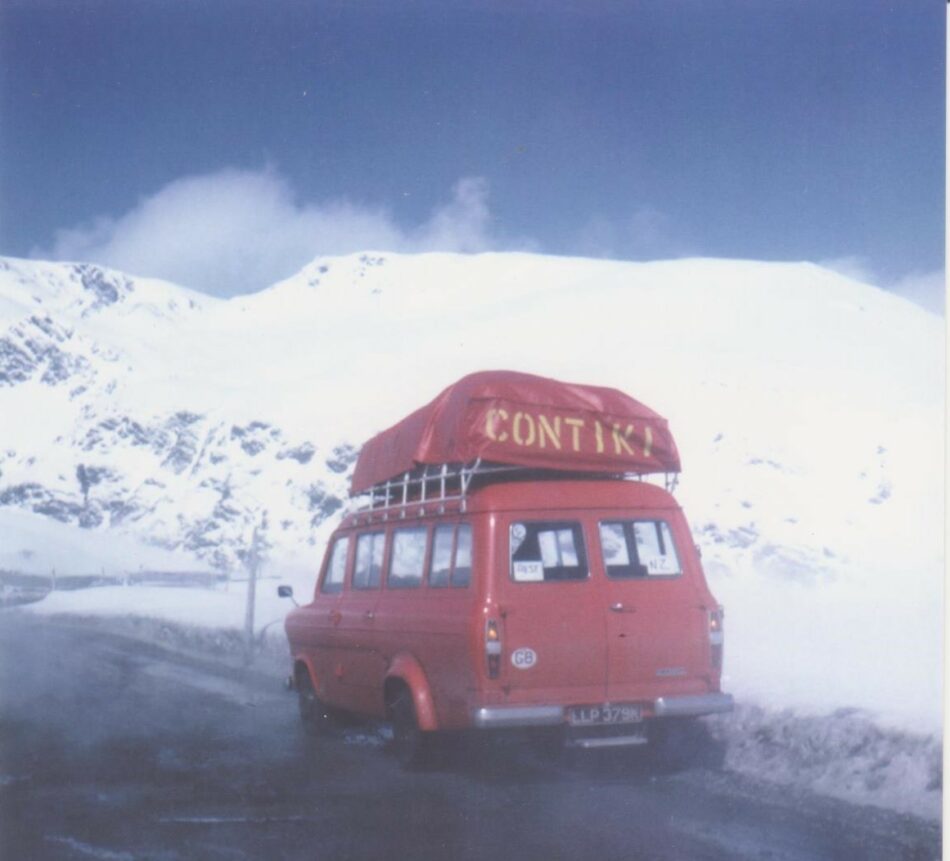 A red van with a tent on top parked on a snowy road during a Contiki reunion.