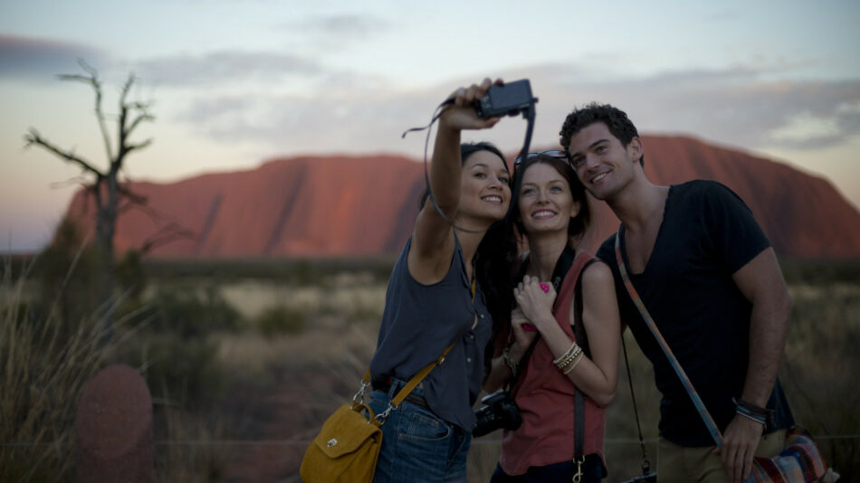 Three people capturing a selfie in front of Uluru, featuring exceptional photo-ops in Australia.