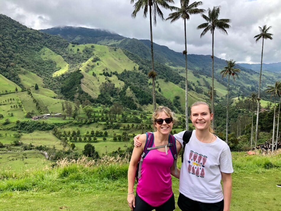 Two women standing in front of a mountain with palm trees.