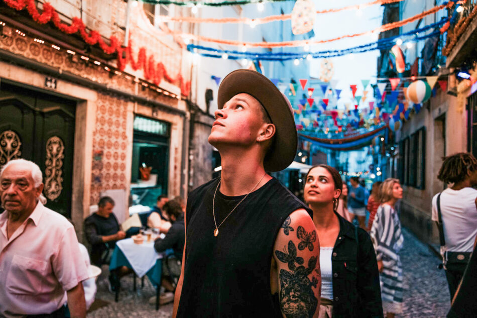 A man in a hat and a woman in a hat walk down a narrow street.