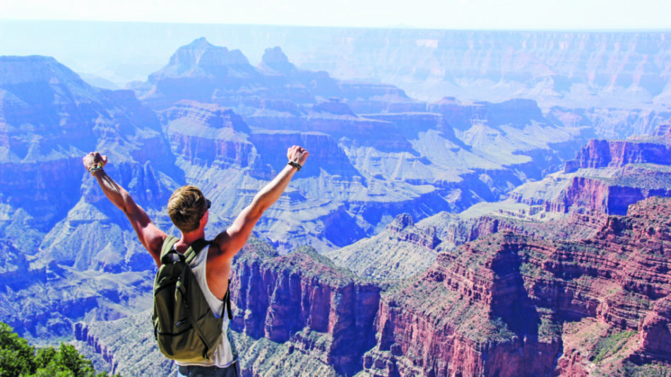 A man enjoying the best drives standing in front of the grand canyon with his arms outstretched.