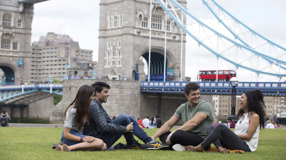 A group of Londoners sitting on the grass in front of Tower Bridge.