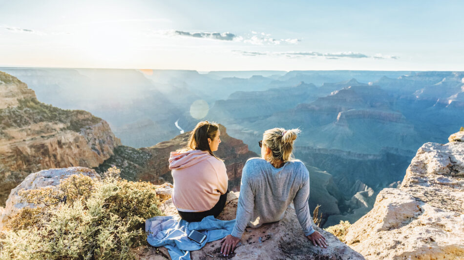 Two women sitting on a cliff overlooking the grand canyon.