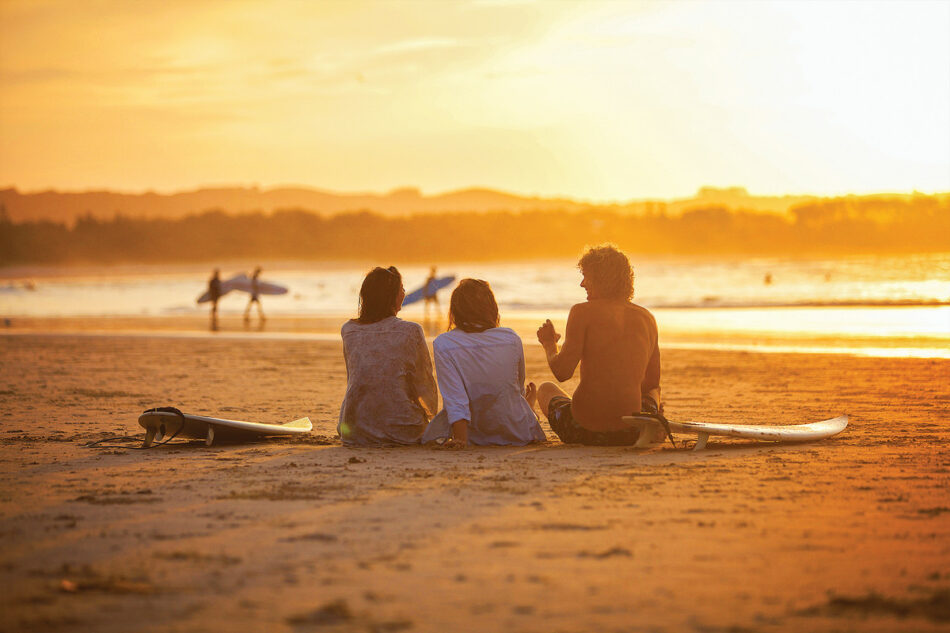 Three surfers at the beach with surfboards.