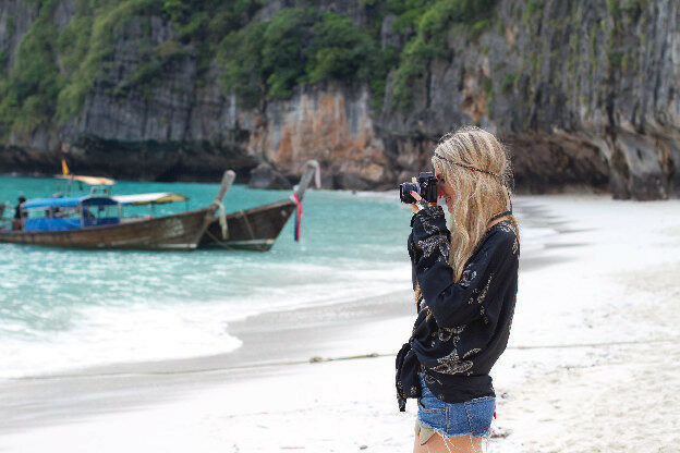 A woman is taking a picture of a boat on the beach.