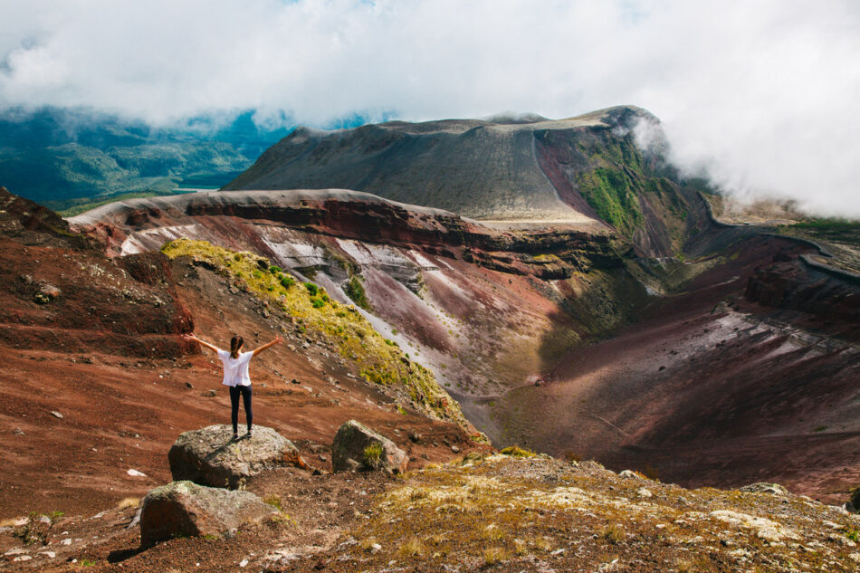 A man standing on top of a mountain with clouds in the background, observing nature's wonders.