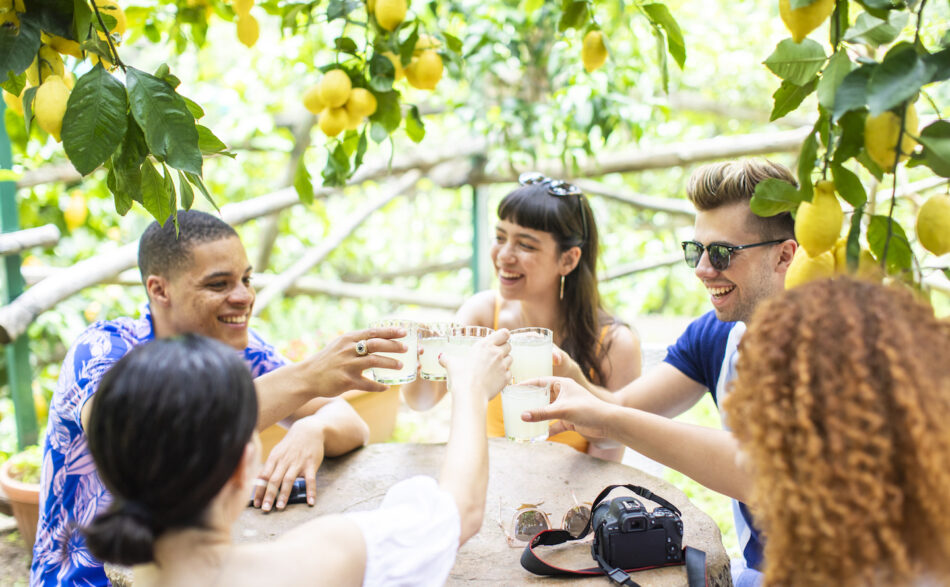 A group of friends toasting at a table under a lemon tree in Europe.