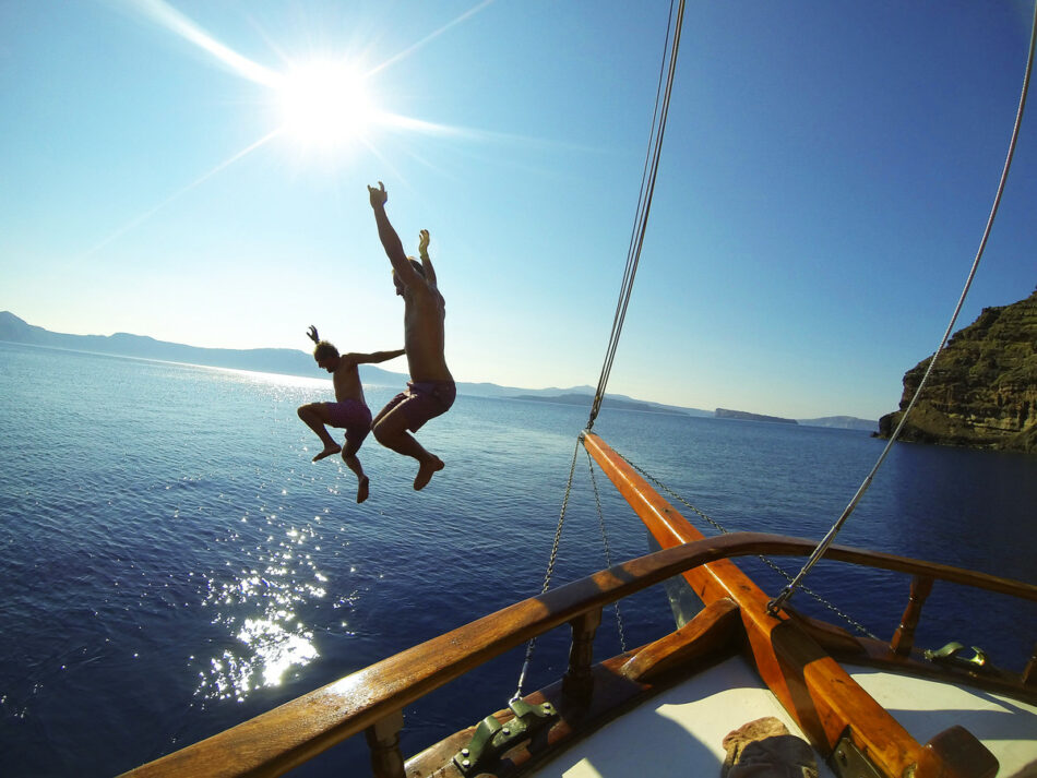 Two people jumping off the deck of a boat in affordable countries.