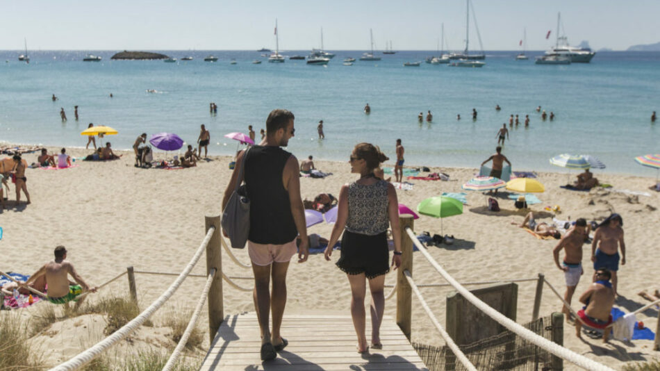 A couple strolling down a wooden walkway on an Ibiza beach.