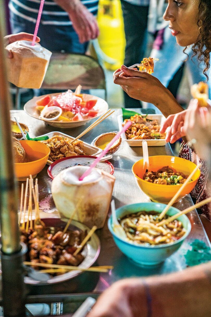 An outdoor market in Asia where a group of people are enjoying delicious food from various vendors.