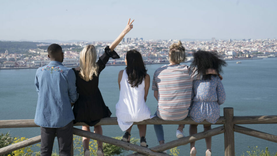 A group of people travelling to Portugal, sitting on a railing overlooking a city.