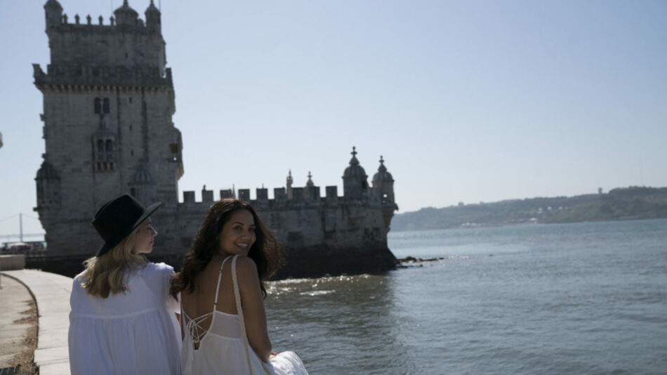 Two women in white dresses standing next to a body of water while travelling to Portugal.