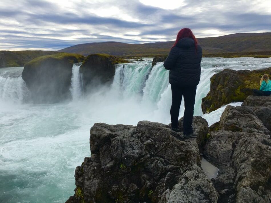 A solo traveler standing on top of a waterfall in Iceland.