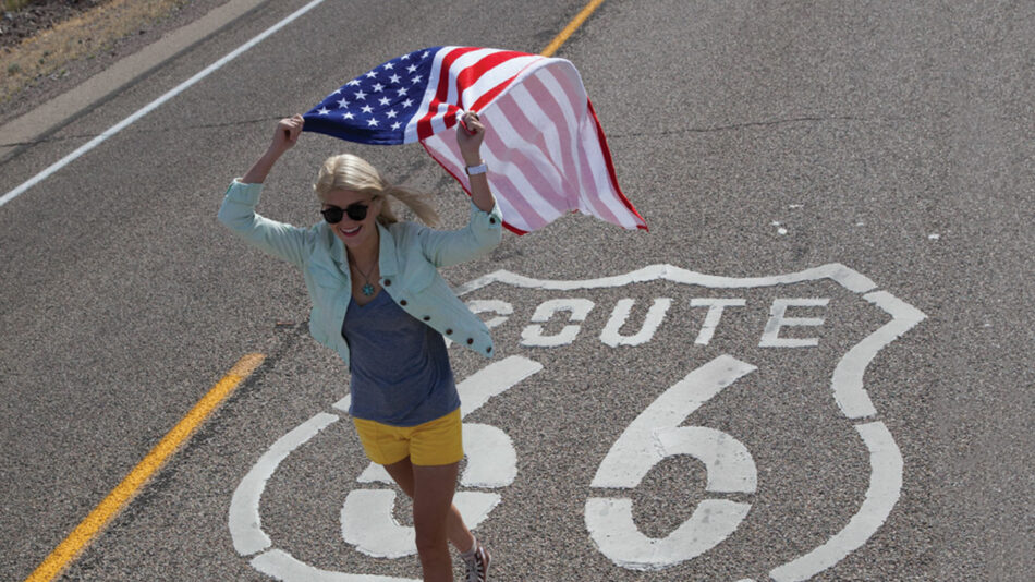 girl walking on route 66 road sign waving flag