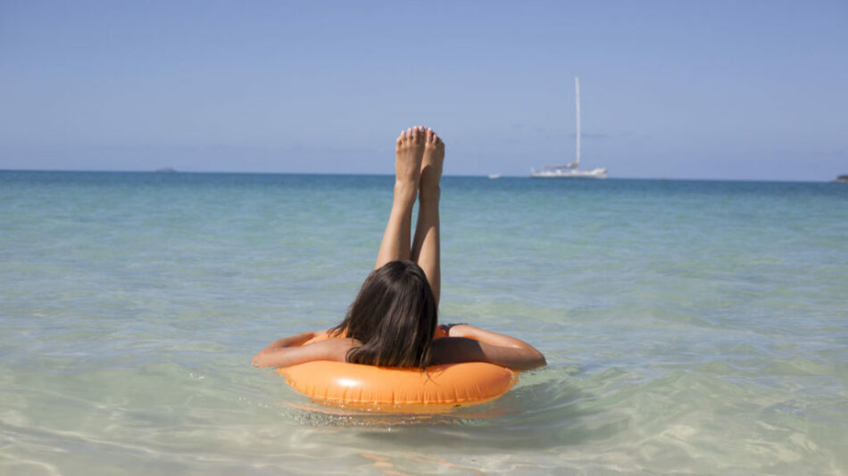 A woman embraces self love as she floats on an orange ring in the ocean.