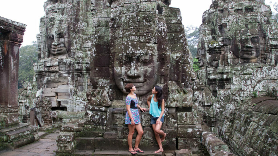 Two women posing in front of a large statue during their South East Asia travel.