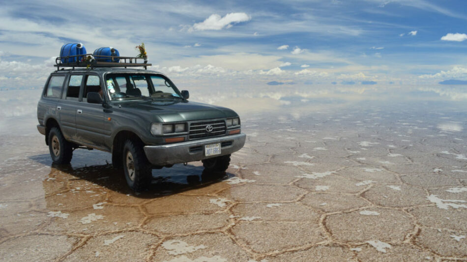 A green SUV is parked in the middle of a Latin American salt flat.