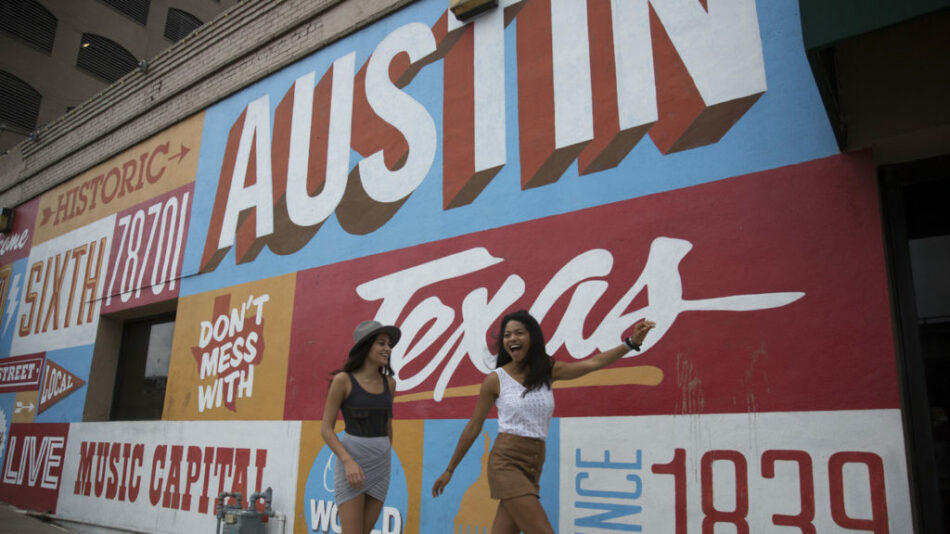 Two women standing in front of a mural of Austin, Texas, a popular music destination.