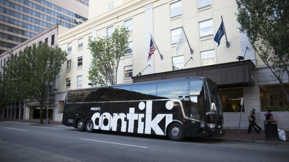 A black and white tour bus parked in front of a building, managed by a Contiki social media manager.