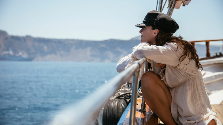 A woman is sitting on the rail of a boat, indulging in her travel addiction.