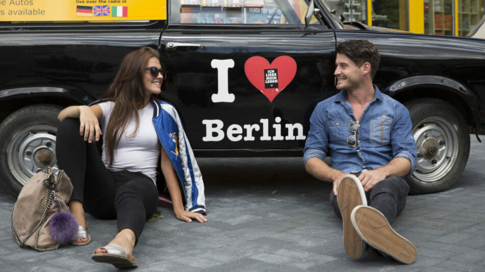 Two people sitting in front of a black car with i love berlin written on it at a music destination.