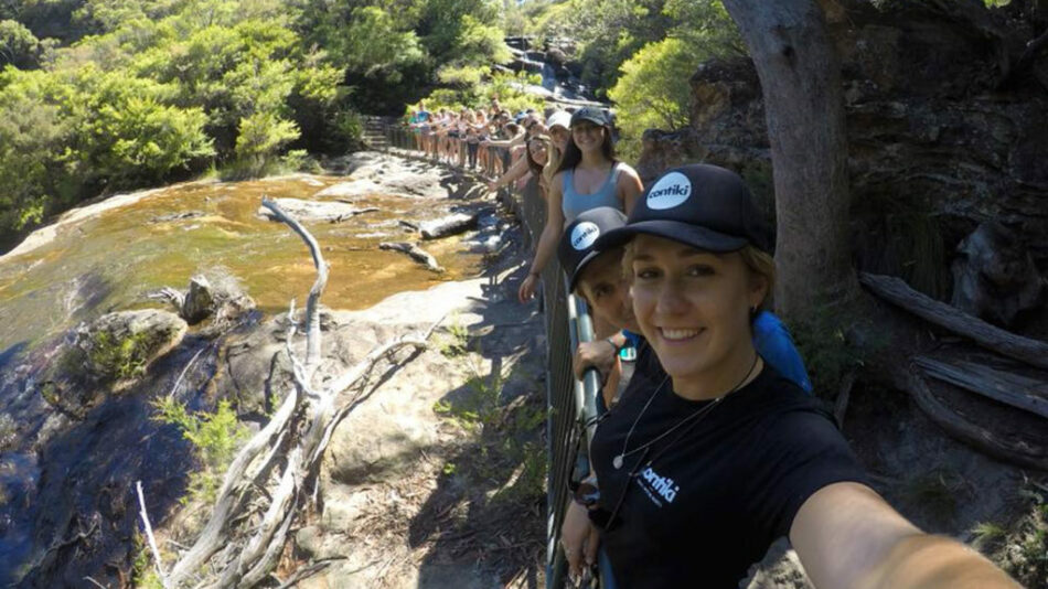 A group of people on a Contiki trip taking a selfie on a bridge over a river.