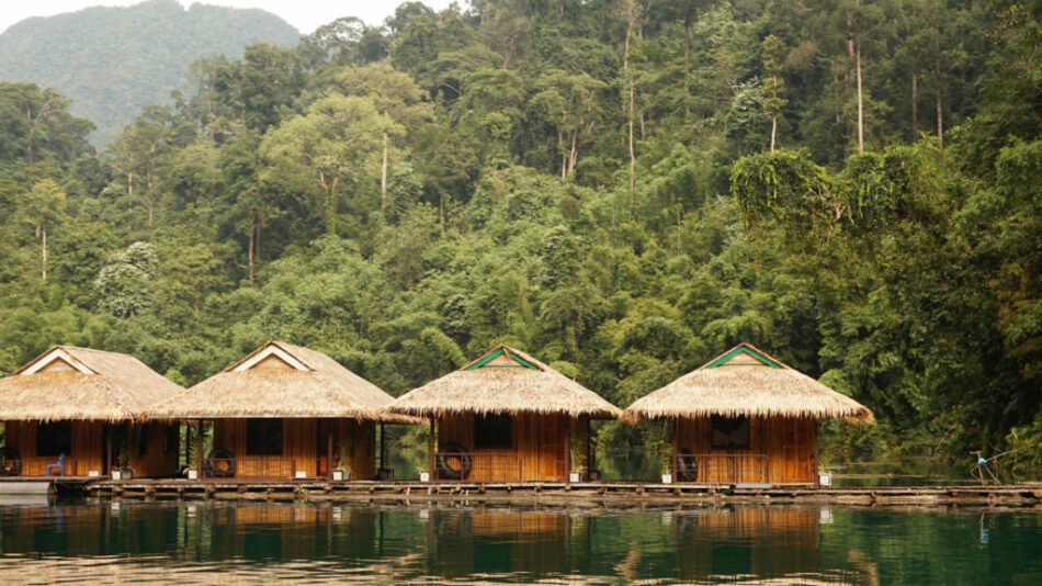 A row of thatched huts on the edge of a Contiki Special Stays lake.