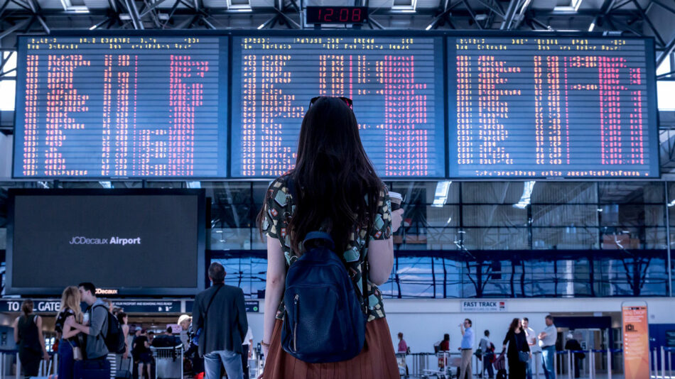 A woman is standing in front of an airport departure board.