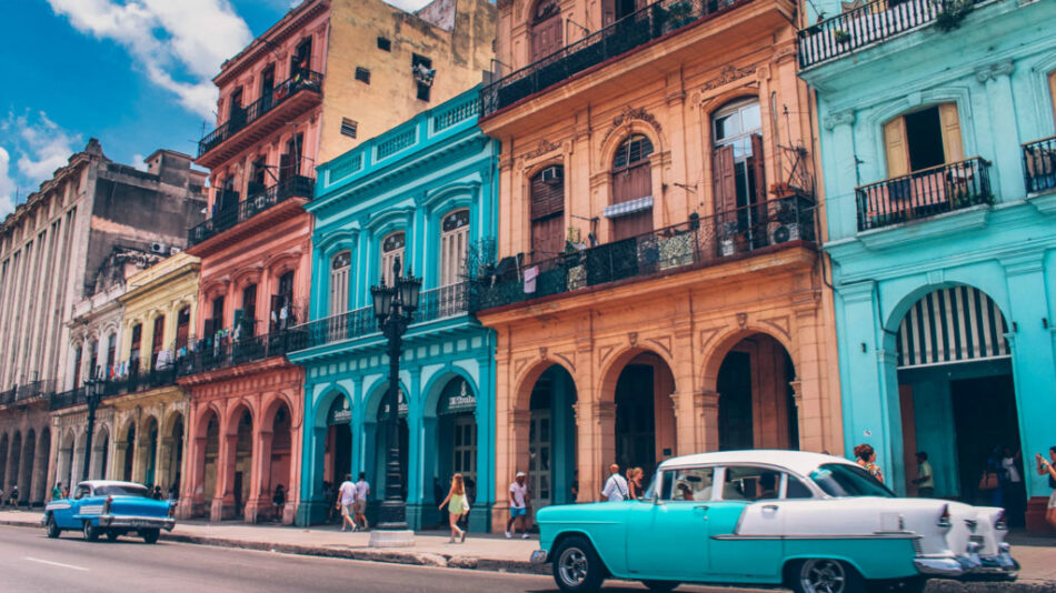 A blue car is parked in front of colorful buildings in Havana, Cuba.