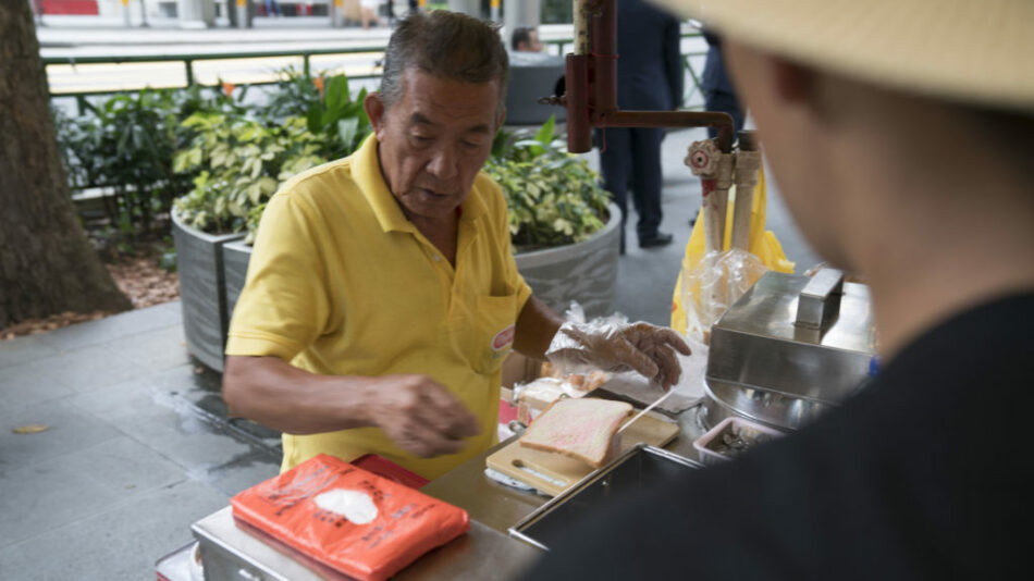 A man in a hat is preparing food for a customer while leaving a coin trail.