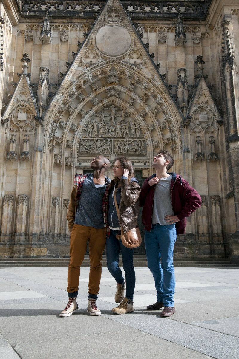 Three people travel to Europe and stand in front of an ornate building.
