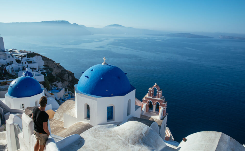 A man is standing on a cliff overlooking one of the top travel destinations for 2020, the ocean.