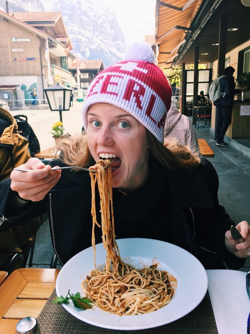 A woman exploring her relationship with food while eating spaghetti and wearing a beanie.