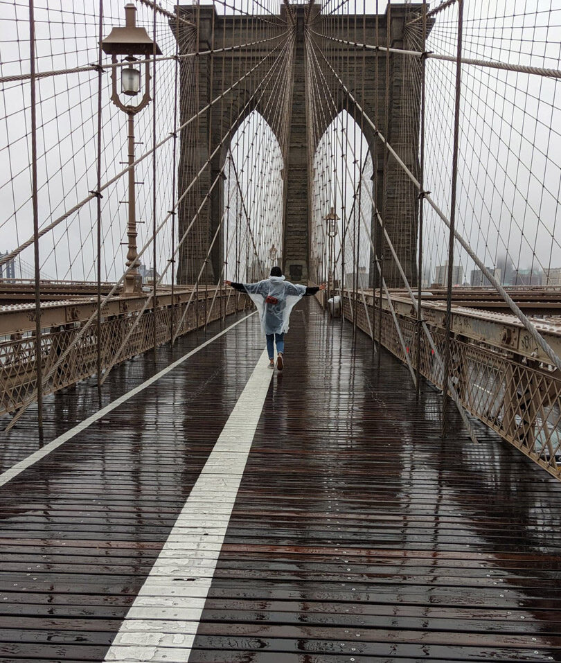 A person standing on the brooklyn bridge in the rain.