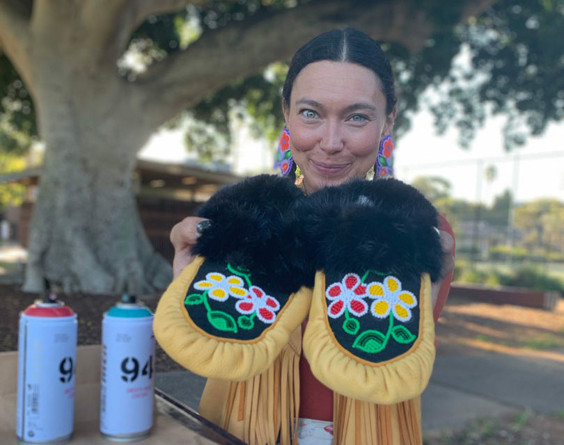 A woman, sarain fox, holding up a pair of moccasins.