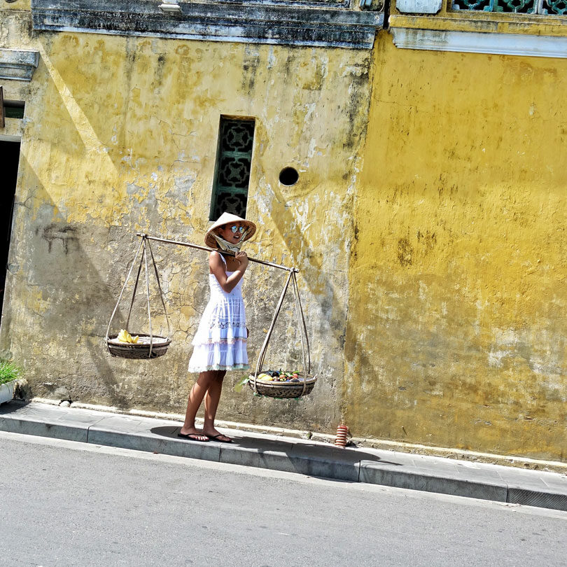 A fashion-forward woman gracefully carries a basket on her head in Hoi An.