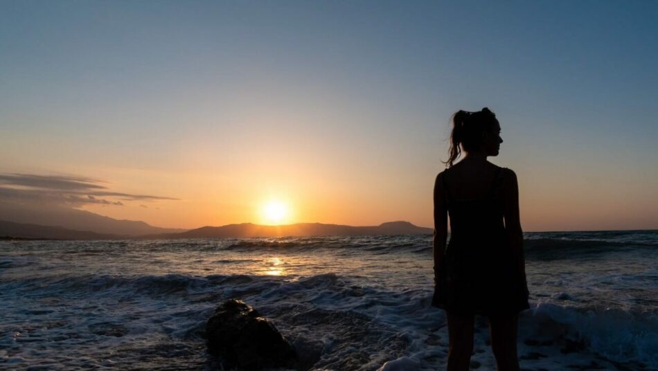 A silhouette of a woman standing on the beach at sunset.