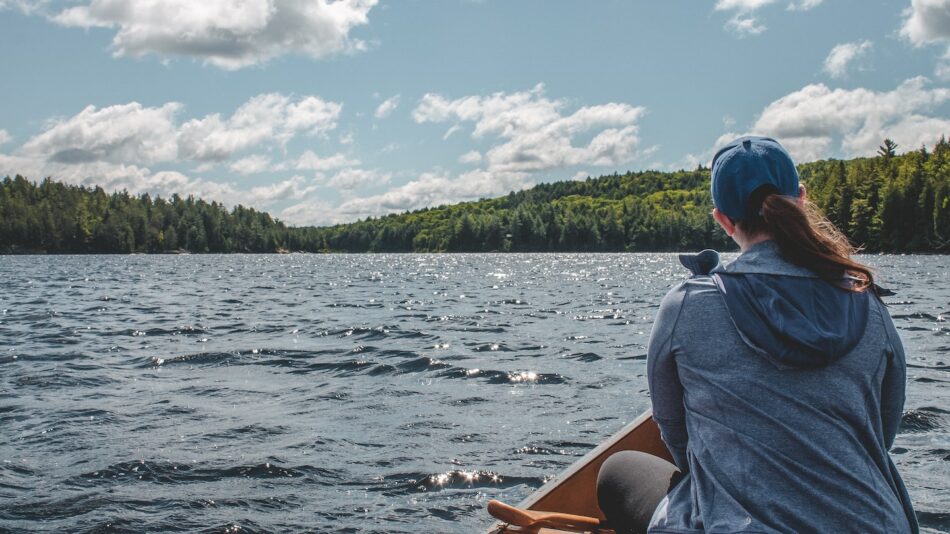 A woman is canoeing on a lake with trees in the background.