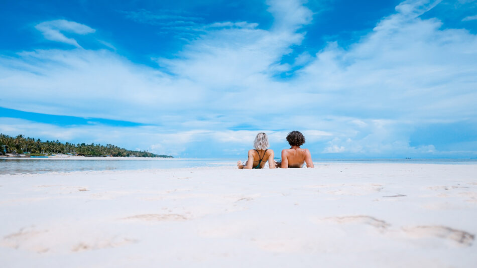 Two people sitting on the sand on a tropical beach.